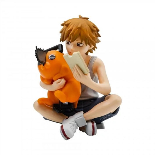 Figurine of a person sitting with an orange creature, holding a book on a white background. Chainsaw Man Denji & Pochita Authentic Break Time Collection Vol.3 Fixed-Pose Interaction Statue by Bandai Banpresto