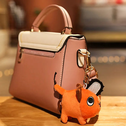 Pink handbag with a keychain shaped like a cartoon dog on a wooden surface. Chainsaw Man Pochita Premium Plush Toy