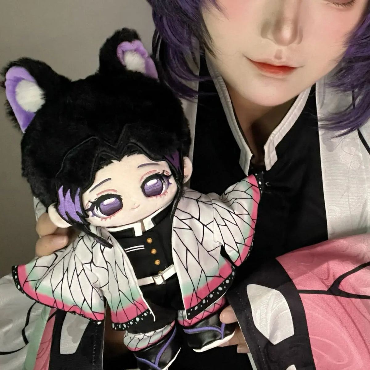Person holding a plush toy with black hair and purple eyes, wearing a black and white outfit. Demon Slayer: Kimetsu no Yaiba Shinobu Kocho Premium 20cm Super Soft Plushie Doll – Fluffy Purple-Eared Animal Hood Edition 2