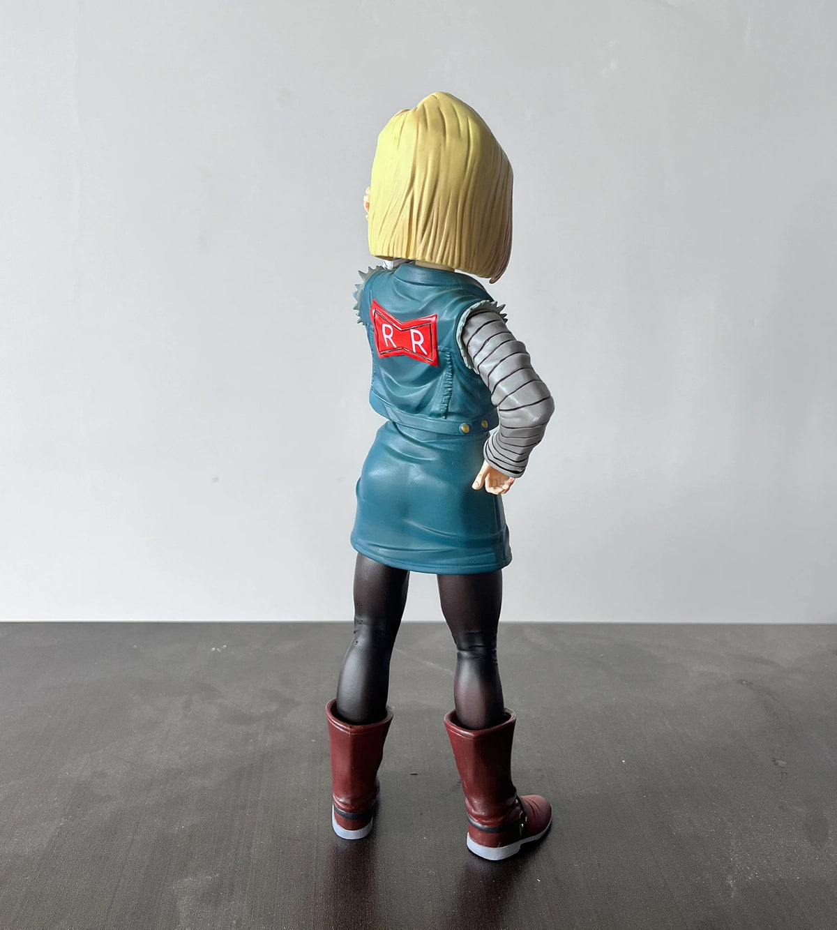 Figure wearing a blue jacket with a red and white logo on a gray floor and white wall background Dragon Ball Z: Android 18 (Lazuli) Premium 11-Inch Statue Figure – Android Saga Classic Denim Outfit Edition