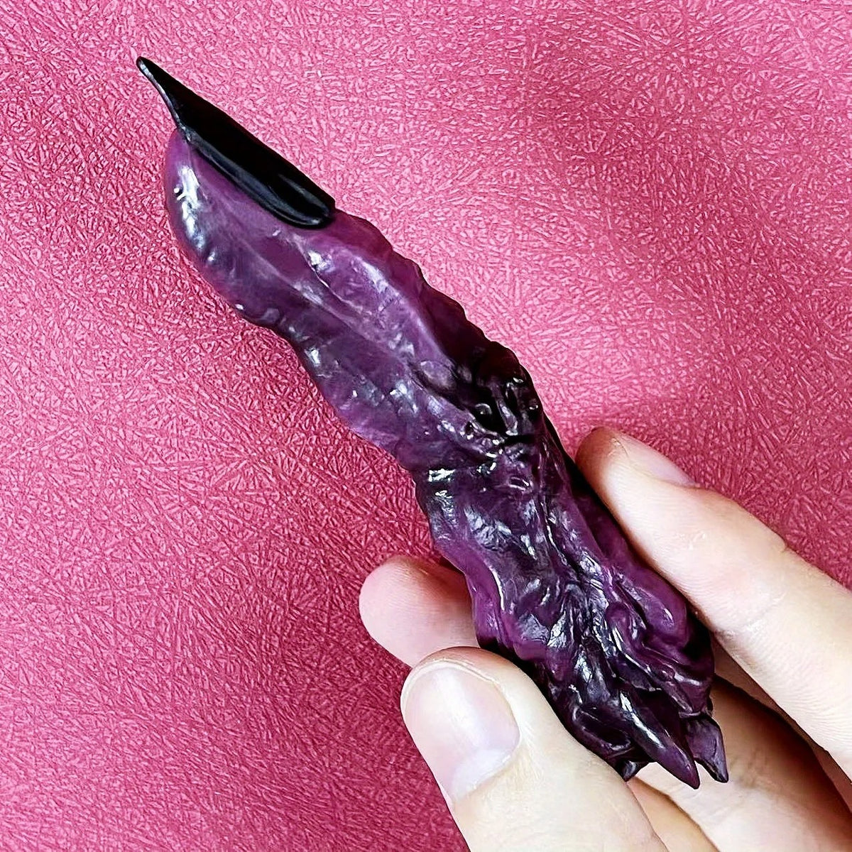 Purple and black object held in a hand against a pink textured background Jujutsu Kaisen Ryomen Sukuna Cursed Finger Authentic Figurine Prop Replica Set – Special Grade Cursed Object Edition with Talisman-Sealed Wooden Storage Box