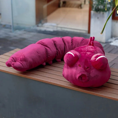 Pink caterpillar-shaped pillow on a wooden surface with a blurred indoor background Jujutsu Kaisen Toji Fushiguro Inventory Cursed Spirit Authentic Huggable Plush Doll – "Ugly Treasure" Special Grade Cosplay Companion & Room Decor Plush