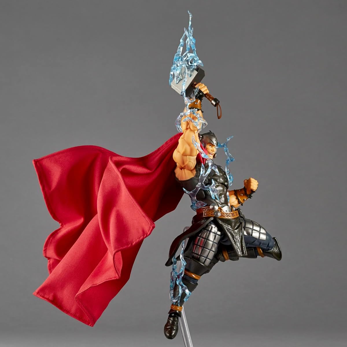 A Thor action figure posed mid-leap with a flowing red cape, black and silver armor, and a blue lightning effect around the raised hammer, photographed against a plain gray studio background. Marvel Amazing Yamaguchi Revoltech NR018 Thor Authentic Action Figure