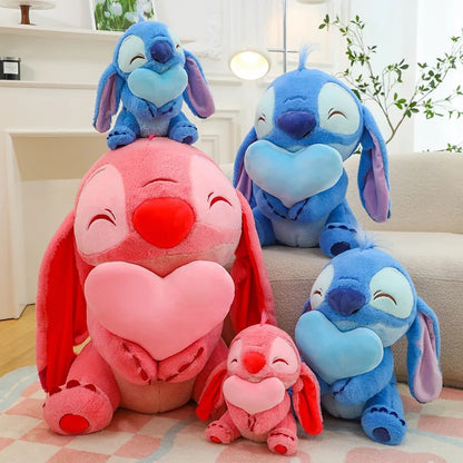 Set of blue and pink plush toys resembling cartoon characters on a light-colored floor. Official Disney Stitch & Angel Hugging Heart Premium Cotton Plush Set by Titantoons