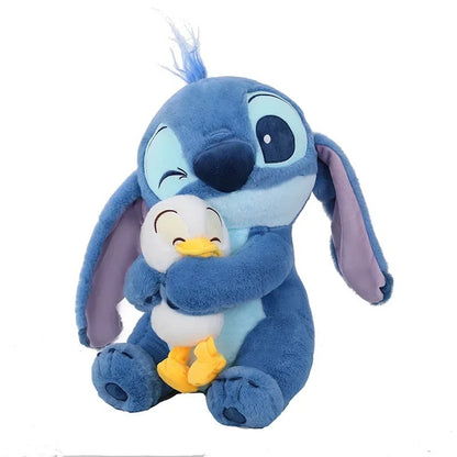 Plush toy of a blue character holding a smaller white and yellow character on a white background Official Disney Stitch Hugging Duck Premium Cotton Plush by Titantoons – Available in 12-Inch, 18-Inch, & 24-Inch