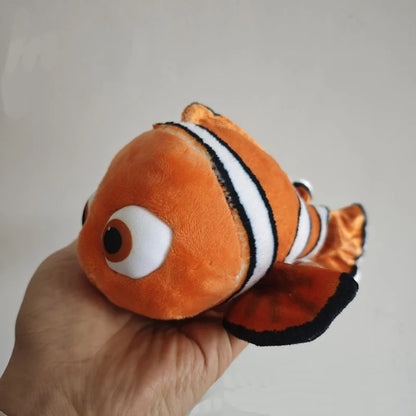 An orange plush fish toy with white and black stripes, held in a person's hand against a plain light gray background. Official Finding Nemo & Dory Premium Best Friends Plush by Titantoons