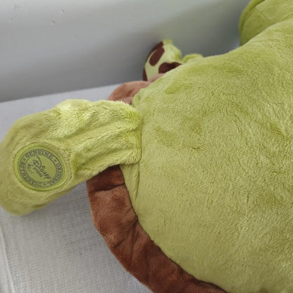 Close-up of a plush toy showing a light green body, a brown underside, and a small round tag that reads Disney Character Toy. Official Finding Nemo Sea Turtle Premium Cotton Plush by Titantoons