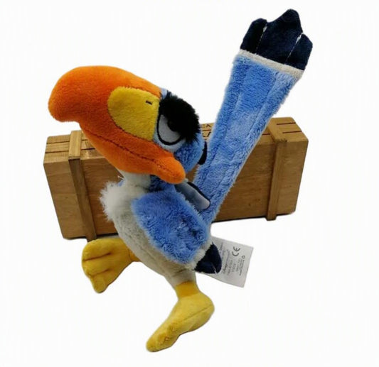 A plush toy of the cartoon hornbill Zonk, featuring a bright orange beak, blue body, yellow feet and chest, and black eye detail, posed in front of a small wooden crate on a white background. Official The Lion King Zazu Premium Cotton Plush by Titantoons