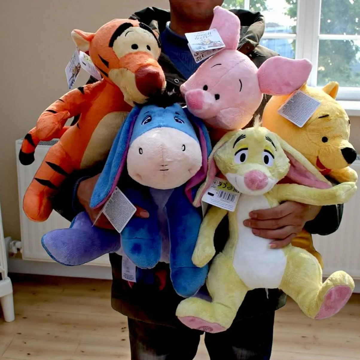 A person holding a large group of plush toys, including Tigger, Piglet, Eeyore, Winnie the Pooh, and Rabbit, with price tags still attached. Official Winnie the Pooh & Friends Premium Cotton Plush Collection by Titantoons