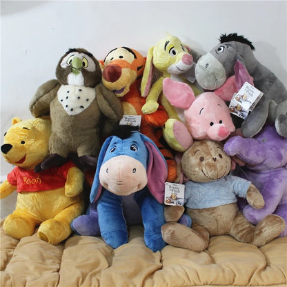 A group of Disney animal-themed plush toys stacked together on a beige blanket, including Winnie the Pooh, Tigger, Piglet, Eeyore, Roo, Totoro, Winnie the Pooh, and Alice. Official Winnie the Pooh & Friends Premium Cotton Plush Collection by Titantoons – Individual Storybook Characters or Complete 9-Piece Heirloom Nursery Set