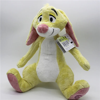 A yellow plush bunny toy with pink inner ears, pink feet, and a white belly, sitting against a light gray studio background. A product tag is attached near the neck. Official Winnie the Pooh & Friends Premium Cotton Plush Collection by Titantoons – Individual Storybook Characters or Complete 9-Piece Heirloom Nursery Set
