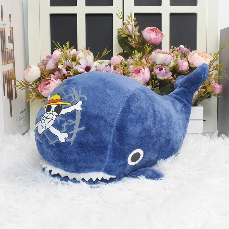 Blue plush whale toy with a character design on a white surface with flowers in the background One Piece: Island Whale Laboon Authentic 25cm Premium Plush Figure