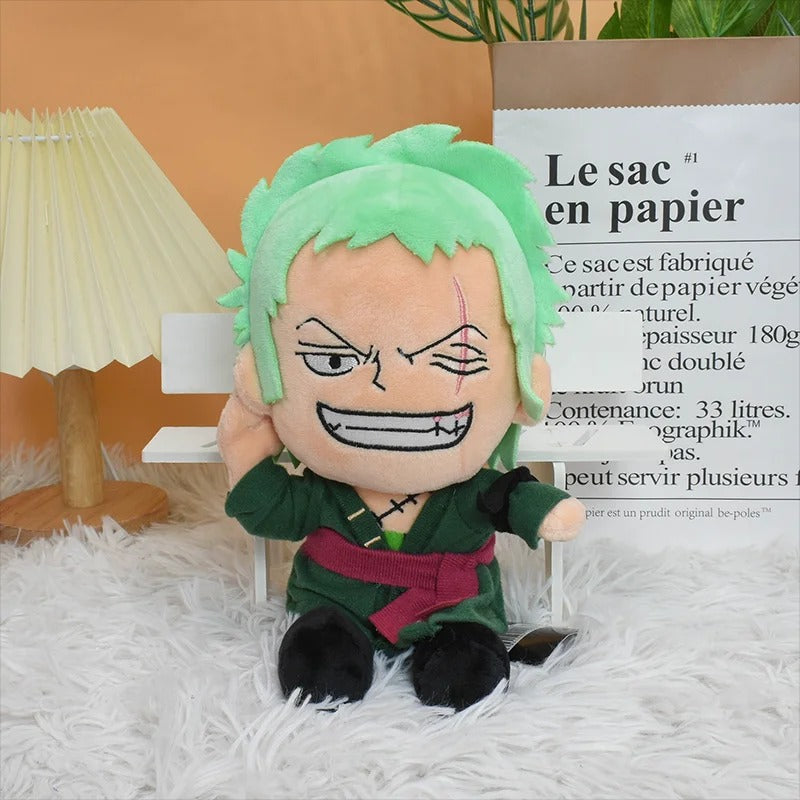 Plush toy with green hair and a red belt on a white surface with a lamp and paper bag in the background. One Piece: Roronoa Zoro Premium 26cm Character Plush