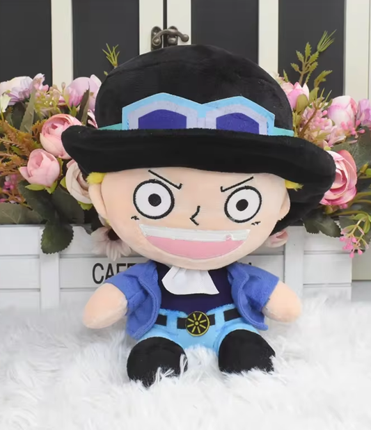 Plush toy of a character with a black hat and blue outfit in front of floral decorations. One Piece: Sabo Authentic Sakami 25cm Premium Plush Figure