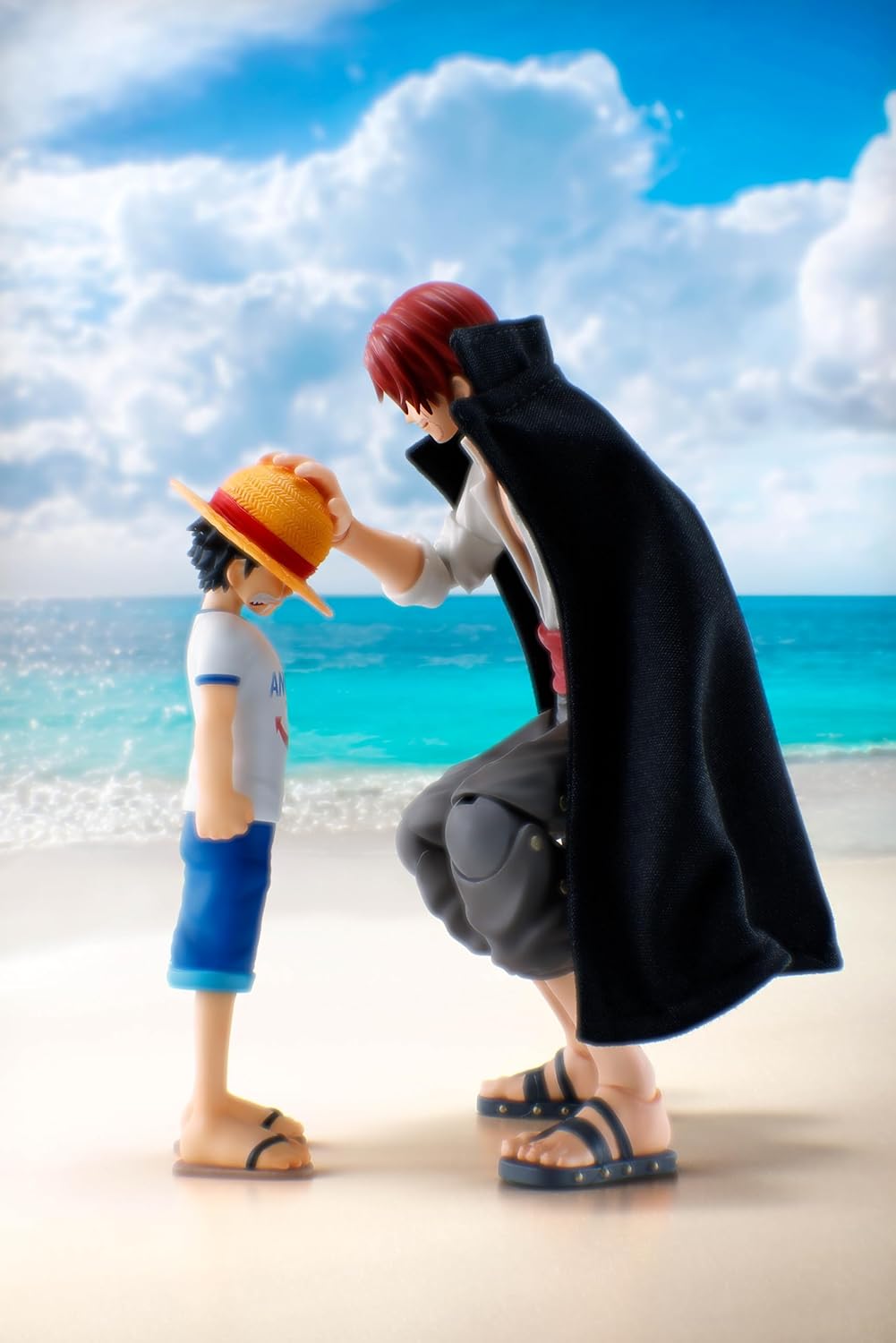 Two figurines on a beach with a blue sky and ocean in the background One Piece: Shanks & Monkey D. Luffy (Childhood Ver.) Authentic S.H. Figuarts Fully Articulated Twin-Pack Action Figure Set by Bandai Spirits