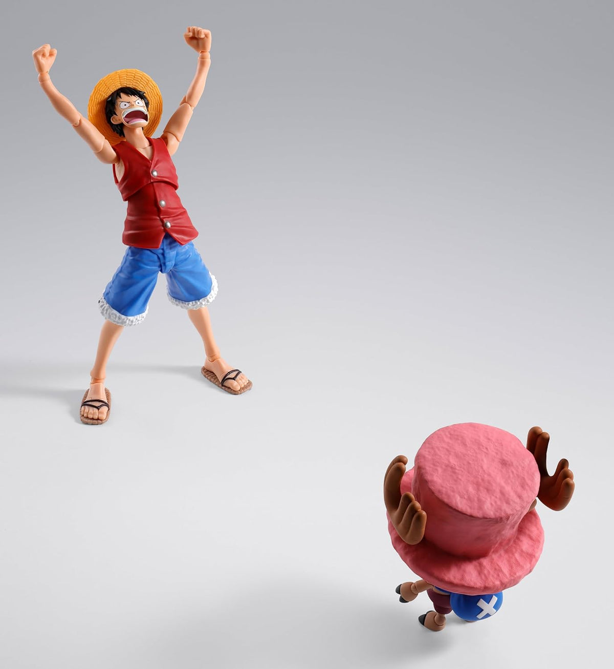 Two action figures, one standing with arms raised and the other sitting on the ground, on a gray background. One Piece: Tony Tony Chopper (Drum Island Ver.) Authentic S.H. Figuarts Fully Articulated Action Figure by Bandai Spirits