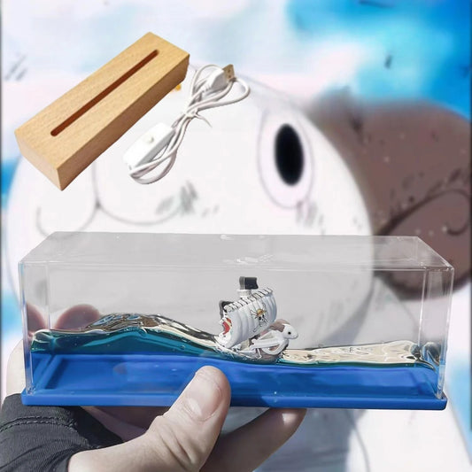 Model of a fish inside a clear box with a blue base, held by a person wearing gloves. One Piece: Unsinkable Ship Liquid Drift Bottle – Thousand Sunny & Going Merry Premium Acrylic Desktop Motion Decor with Separate USB LED Illuminating Base