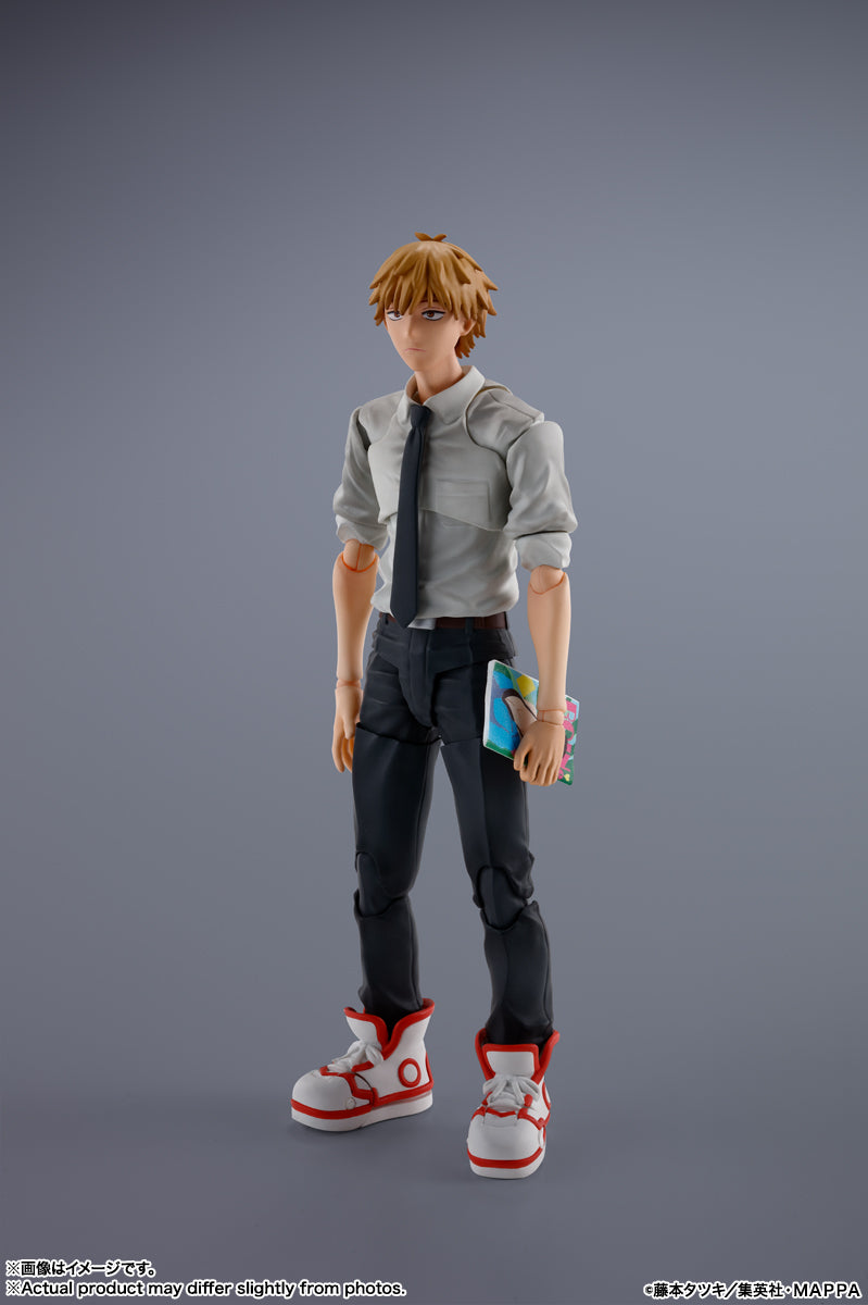 Action figure of a character with orange hair and glasses, wearing a gray shirt and black pants, holding a blue object on a gray background. S.H.Figuarts Denji Authentic Action Figure – 5.9-Inch Human Form Fully Articulated Premium Collectible with Pochita Figure by Bandai Tamashii Nations front