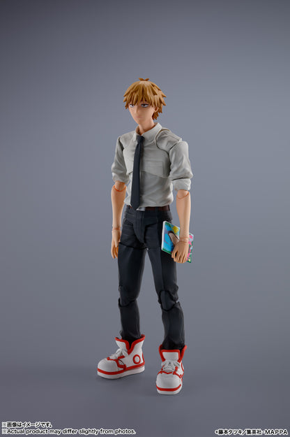 Action figure of a character with orange hair and glasses, wearing a gray shirt and black pants, holding a blue object on a gray background. S.H.Figuarts Denji Authentic Action Figure – 5.9-Inch Human Form Fully Articulated Premium Collectible with Pochita Figure by Bandai Tamashii Nations front