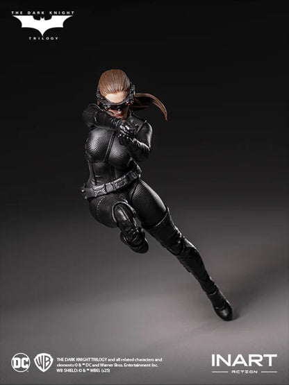 Action figure of a character in a black suit with a helmet, posed on a gray background, featuring logos for The Dark Knight Trilogy and INART Action.