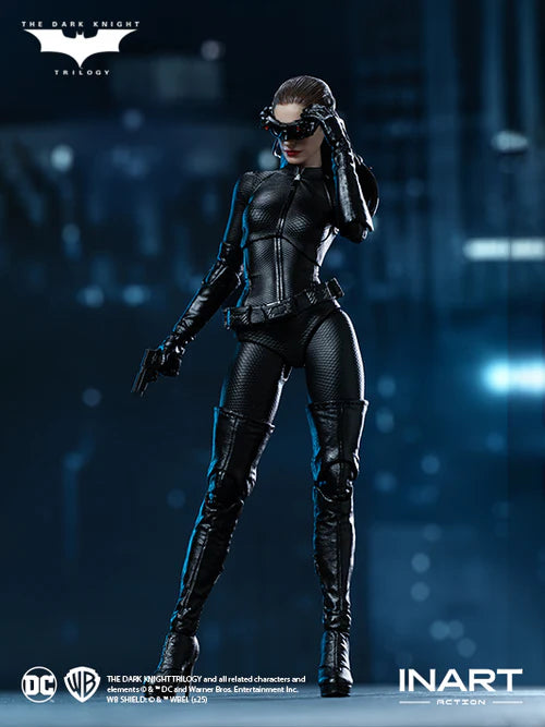 Inart Batman Catwoman collectible action figure in a black textured suit and mask, posed against a dark blue futuristic city background with The Dark Knight Trilogy and Inart logos visible.