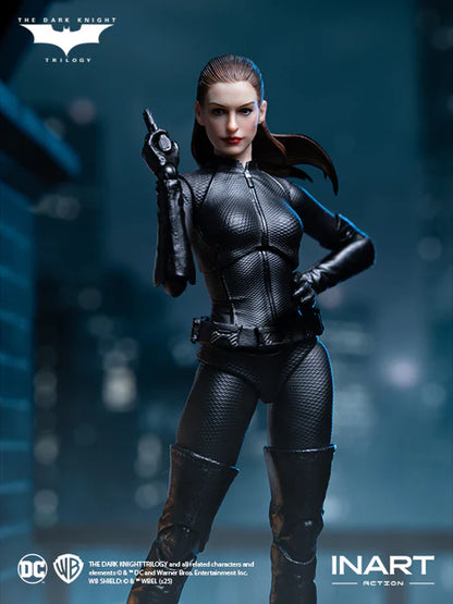 Inart Batman crouching figure from The Dark Knight Trilogy, wearing a textured black suit, posed with one hand on her hip and the other pointing upward, set against a dark, blurred city background. The Dark Knight Trilogy, DC, Warner Bros.